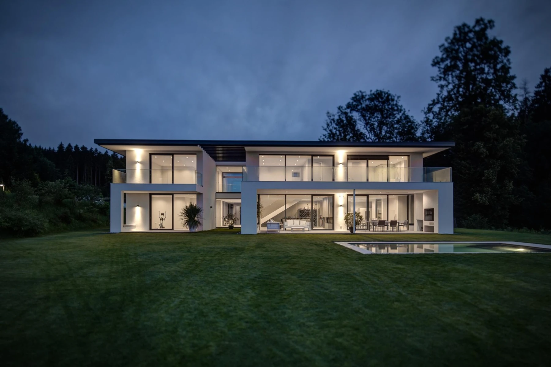 Modernes privates Wohnhaus mit beleuchteten Wohnräumen und Garten in der Abenddämmerung